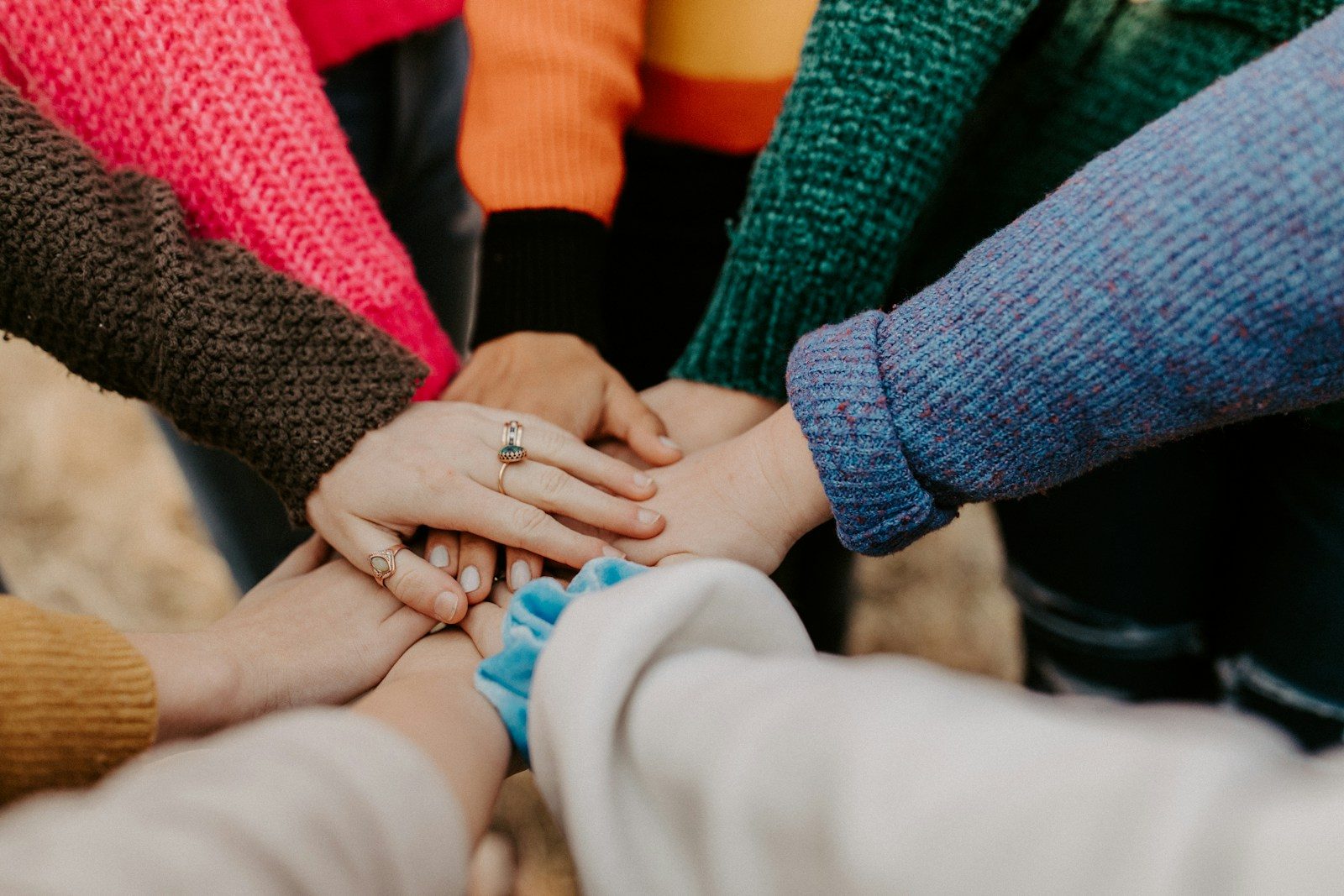 Photo by Hannah Busing group stacking hands in colorful sweaters